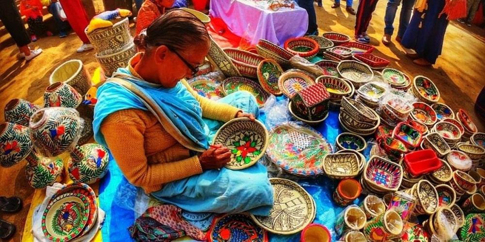 A lady doing painting work on wooden fruit basket at Surajkund international crafts Mela